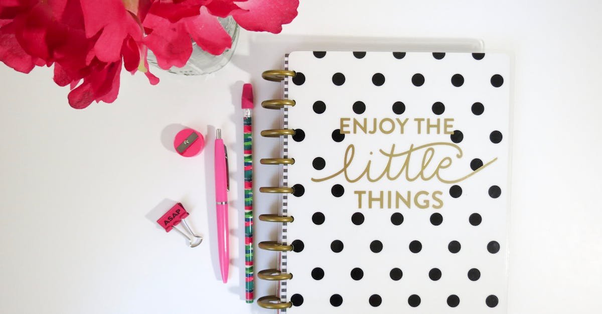 Flat lay of polka dot notebook, flowers, and stationery on white desk.